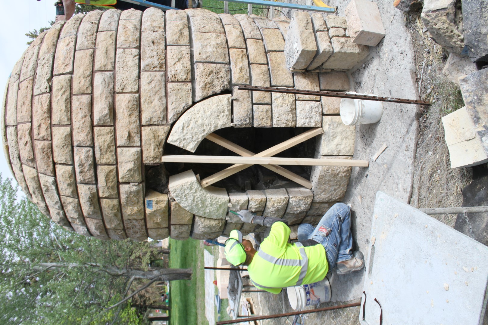 Stone “beehive” fireplace with mason installing new stones in arched opening where stones are missing