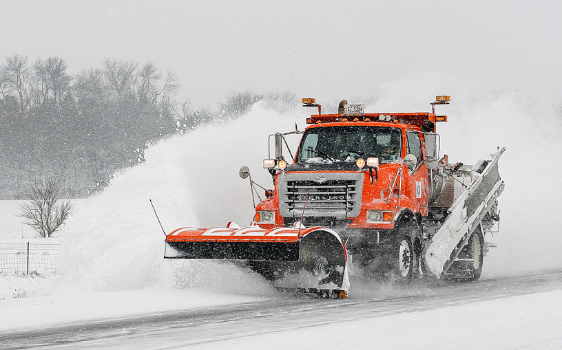 Orange MnDOT snowplow clears a rural highway during a snow storm