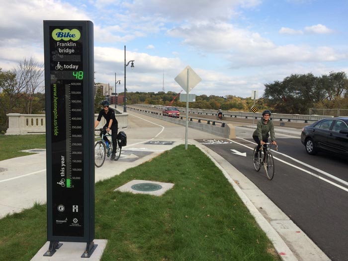 Two bicyclists approaching a bicycle counter at the Franklin Avenue bridge in Minneapolis.